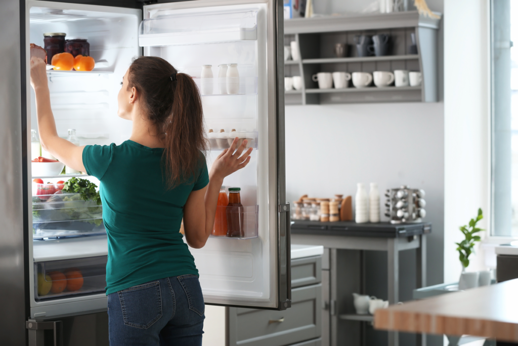 Woman opening refrigerator in her Cayman Islands' kitchen to grab food.