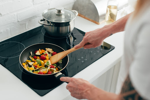 Homeowner cooking vegetables on induction stove while water boils in a pot.