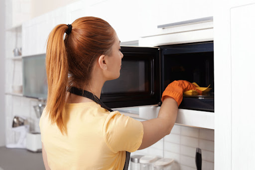 A woman cleaning the inside of a microwave with a rag.