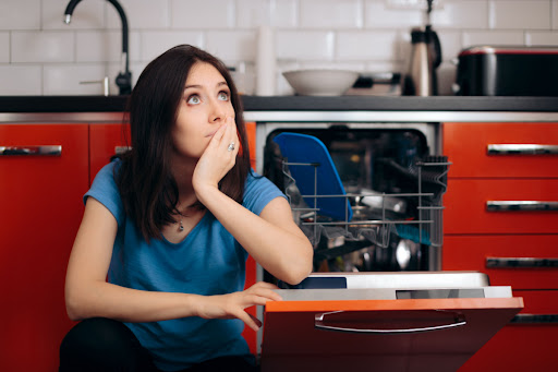 A woman thinking next to an open dishwasher.