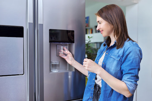 A smiling water filling a glass of water at a refrigerator water dispenser.