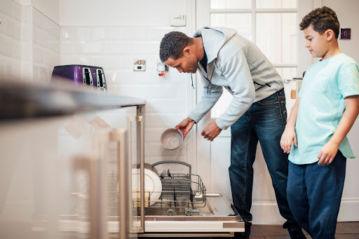 A man and child loading a dishwasher in a kitchen.