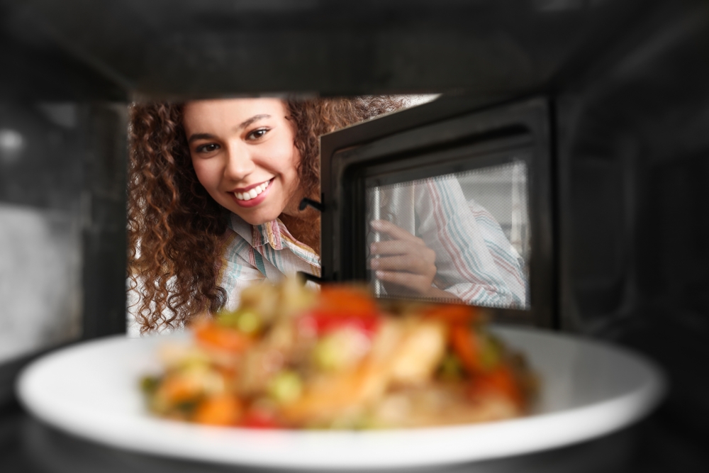 Woman smiling as she looks at the plate of hot food inside her microwave.