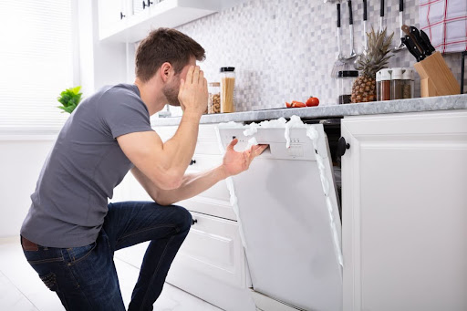A man looking at a dishwasher with suds coming out of it.