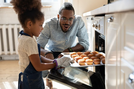 A father and daughter baking muffins in an oven.