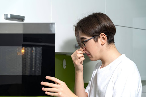 Man holding nose from burning smell in microwave.