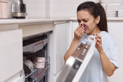 Homeowner plugging nose as she opens dishwasher from stinky stench.